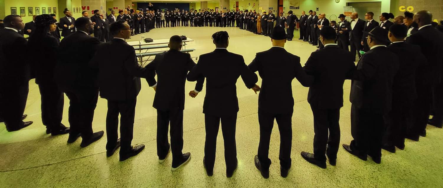 Hundreds of men and boys in tuxedos filling an auditorium