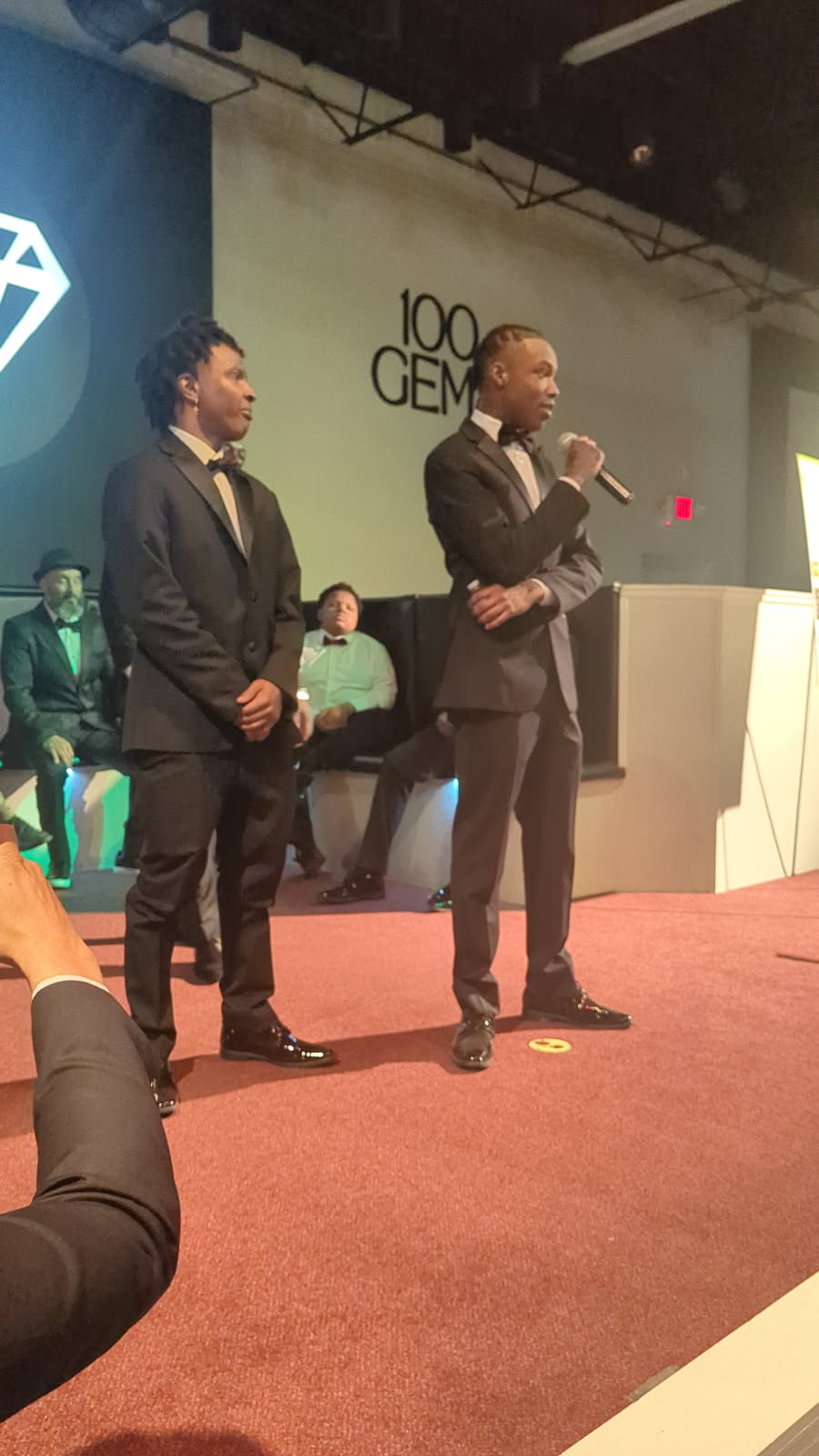 Young men speaking on stage in tuxedos